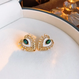 Detailed macro view of heart-shaped vintage gold earring with green gemstone and pearls