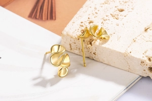 Macro shot of gold spiral leaf stud earrings on beige stone with polished finish