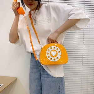 Detail view of a bright orange patent leather crossbody bag in a vintage telephone shape