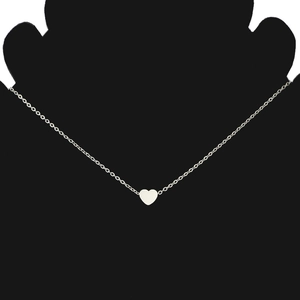 Close-up of a polished silver heart pendant on a thin chain over a black silhouette stand