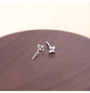 Detailed view of silver square-cut zircon studs on a textured wooden jewelry tray