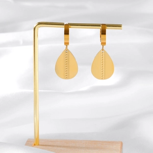 Elegant gold teardrop earrings with textured dots on a silk background with metal stand