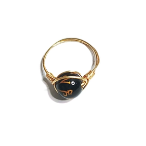 Close-up of handmade gold-wired ring featuring a black bead with golden character detail