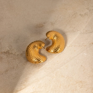 Detail of 18k gold earrings featuring intricate fish scale texture on a stone surface