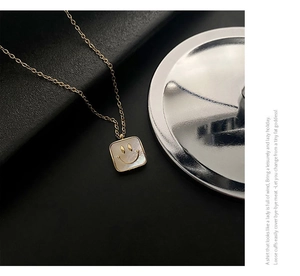 Close-up of golden square necklace with natural shell inlay and a smiling face pendant