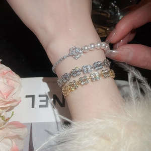 Detail of elegant zircon flower and pearl bracelets layered on a model's wrist