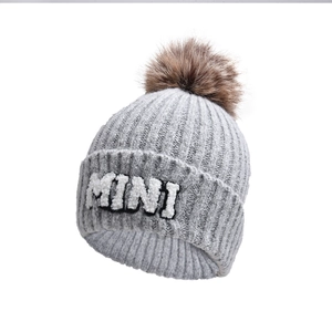 Detail of grey knit hat with MINI lettering and fluffy brown faux fur pom pom