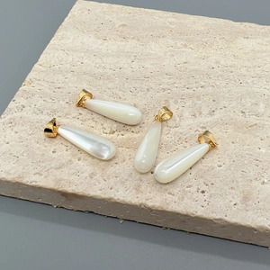 Colgantes de gota de nácar blanco con enganches dorados sobre una losa de piedra natural