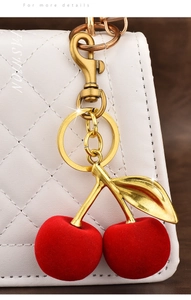 Detail of red flocked cherry keychain pendant on a white quilted handbag with golden leaf