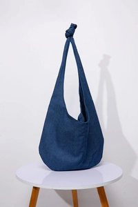 Detail of a dark blue denim hobo bag featuring a stylish knotted shoulder strap on a table