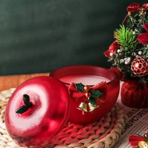 Bougie rouge en forme de pomme avec nœud et cloche dorée sur un tapis tissé élégant