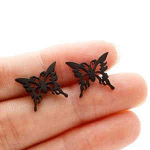 Macro view of matte black butterfly studs on fingers showing detailed hollow engraving
