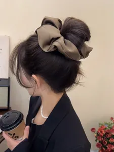 Close-up of oversized olive green satin scrunchie worn in a sleek bun hairstyle