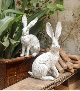 Detail of vintage resin rabbit sculptures with white weathered finish in a garden setting