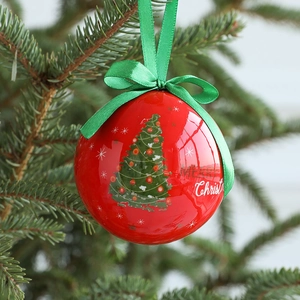 Red Christmas ball ornament with green ribbon bow and Merry Christmas text on pine tree