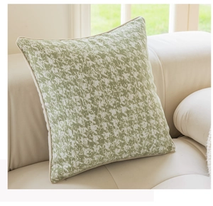 Detail of green and beige jacquard square pillow with piping on a cream leather sofa