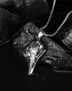 Detailed shot of a silver Viking raven skull pendant with Nordic compass on dark wet rock