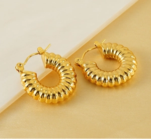 Macro detail of 18K gold plated hoop earrings with textured spiral design on marble