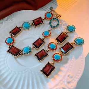 Detail of vintage gold necklace and earrings with red and blue stones on white ceramic tray