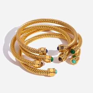 Detailed close-up of three gold cable twist bangles with colorful gemstone end caps