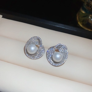 Macro shot of silver pearl earrings with zircon swirl design on soft leather display