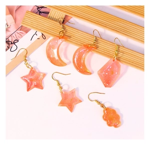 Detail view of handmade resin earrings with orange glitter stars and moon shapes
