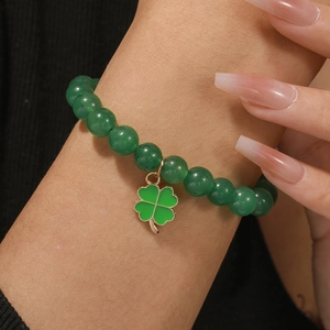 Detail of green natural stone bead bracelet with gold-framed four-leaf clover charm on wrist