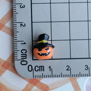 Miniature orange pumpkin charm with black wizard hat shown on grid ruler for scale