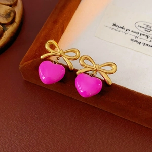 Détail de boucles d'oreilles nœud doré avec pendentifs cœur magenta sur plateau cuir