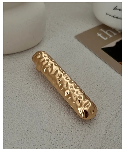 Detail of a minimalist gold metal hair clip featuring a textured hammered finish surface
