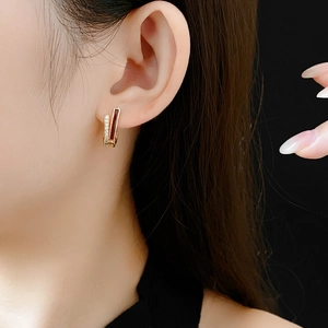 Gros plan sur une mini créole dorée avec pierre rouge rectangulaire et zircon sur l'oreille