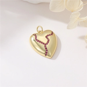 Close-up of a golden heart pendant with a red gemstone inset on a white surface