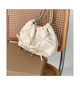 Detail of creamy white PU leather pleated shoulder bag with chic bow accents and chain strap