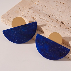 Close-up of blue marbled acrylic earrings with gold metal studs on a stone pedestal