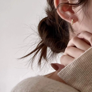 Minimalist knot design hoop earrings in golden finish worn by model in a soft warm setting