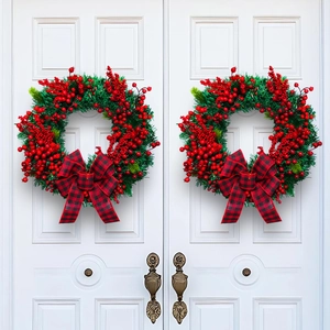 Christmas wreath with green pine needles, red berries and plaid bow on white doors