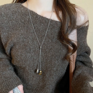 Detail of adjustable Y-shaped long necklace with bicolor teardrop pendants on brown sweater