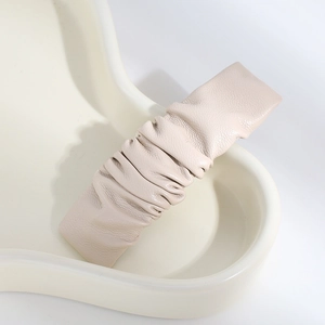 Detail of a beige pleated PU leather hair clip placed on a white ceramic tray