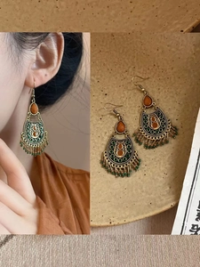 Détail de boucles d'oreilles bohèmes avec métal bronze, perles d'ambre et pompons