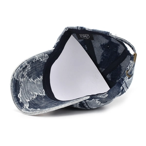 Détail d'une casquette en denim bleu délavé avec trous usés et boucle en métal réglable