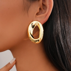 Close-up of a large gold oval stud earring with hammered texture on a model's ear