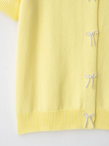 Close-up of bright yellow knit cardigan featuring white pearl bow embellishments