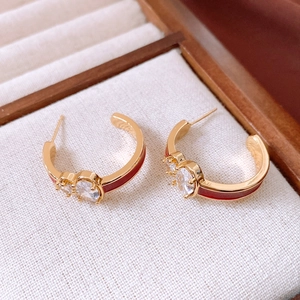 Macro detail of 18k gold-plated C-shaped earrings with red enamel and clear cubic zirconia