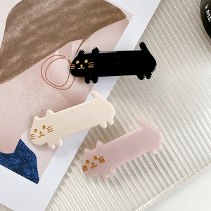 Three acetate cat-shaped hair clips in black, beige, and pink colors on glass tray