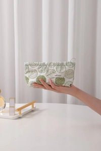 Close-up of green leaf embroidery and brand label on white linen makeup bag