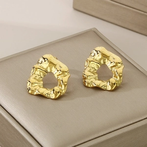 Macro shot of gold irregular wrinkled earrings on a satin surface with light and shadow