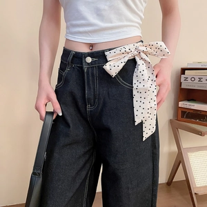 Dettaglio di una cintura a sciarpa beige a pois annodata a fiocco su jeans blu scuro