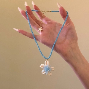 Detail of blue beaded necklace with white shell flower pendant and starfish charm on chain