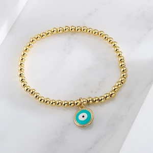 Gold beaded stretch bracelet featuring a turquoise evil eye charm on marble surface