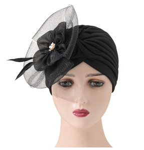 Detail of black turban hat with mesh flower, feathers and white pearls on white background